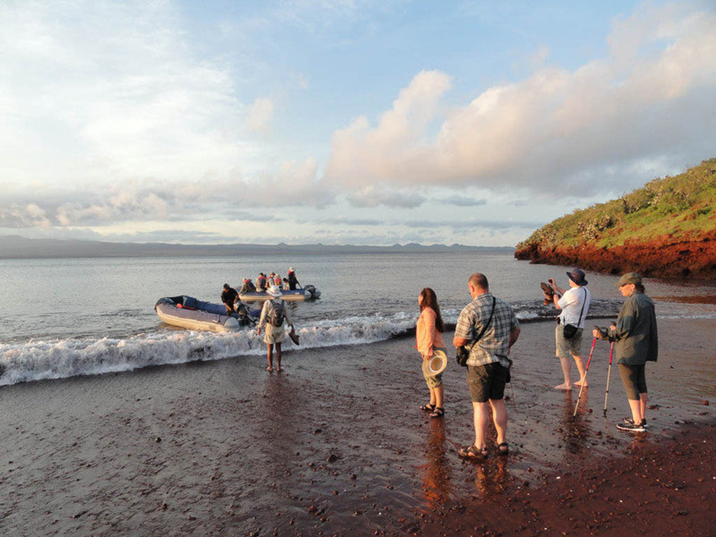 Reizigers stappen vanaf een rubberboot aan op een zwart strand op de Galapagoseilanden tijdens een groepsrondreis.