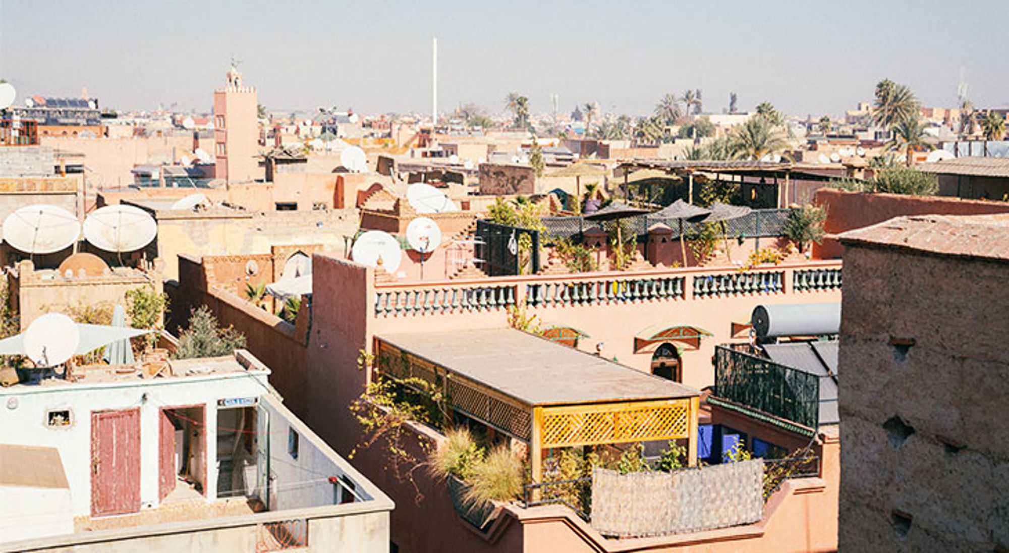 Uitzicht over de daken van Marrakech met terrassen, satellietschotels en palmbomen.