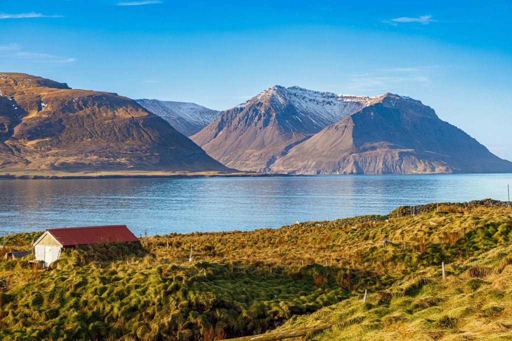 Berglandschap aan een fjord in IJsland met besneeuwde toppen en een huisje in de voorgrond.
