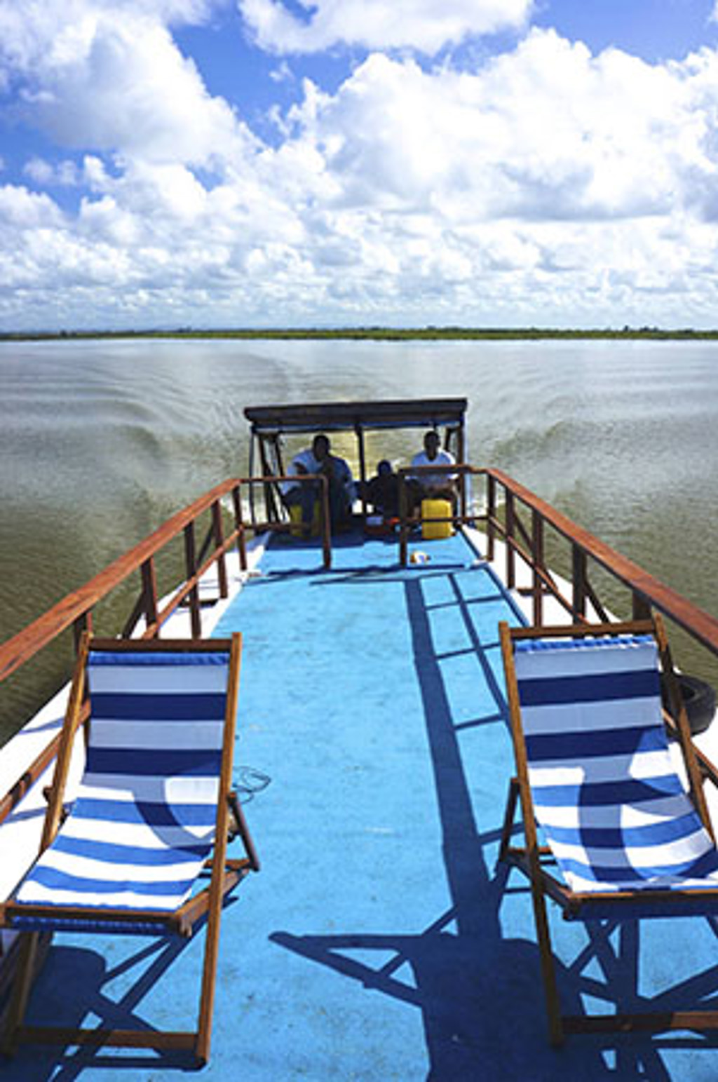 Boottocht over de rivier tijdens een familiereis Madagascar, met ligstoelen op het dek en weids uitzicht.