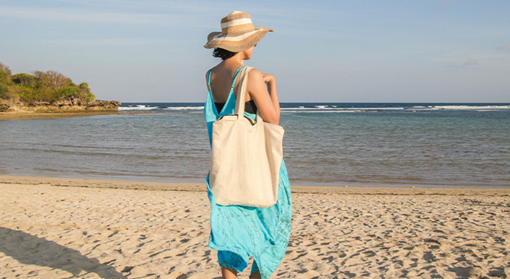 Linnen tasje op reis Vrouw met zonnehoed en strandtas loopt over het strand langs de zee.