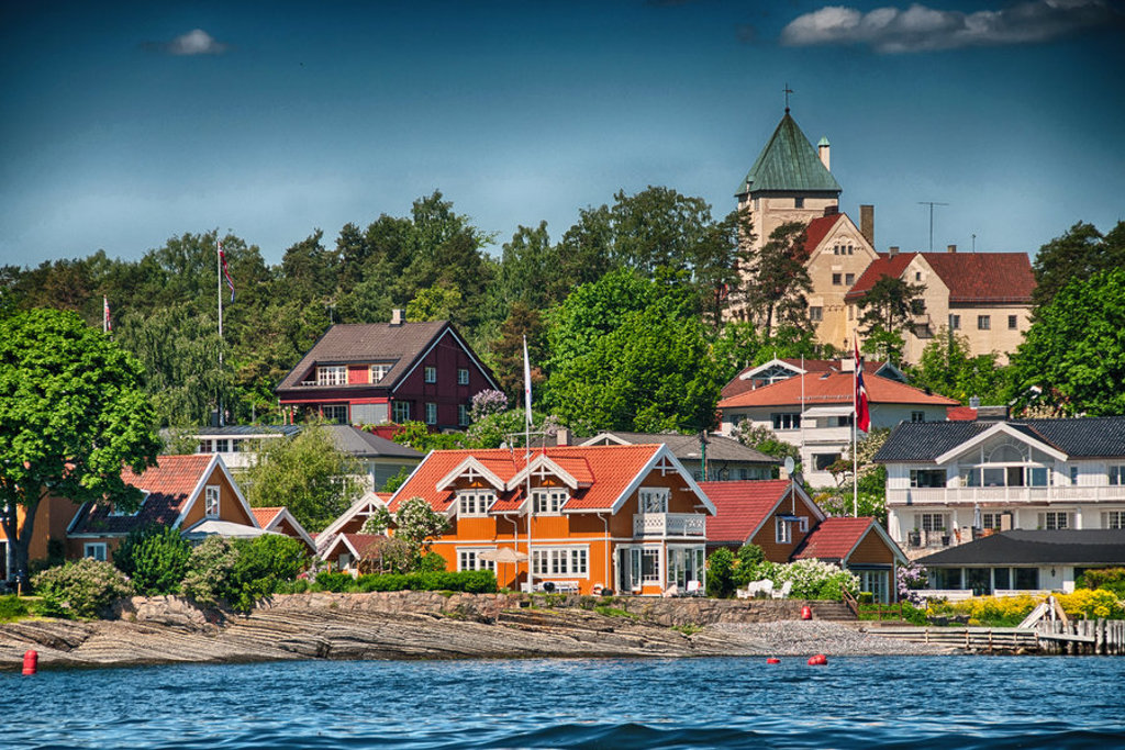 Kleurrijke houten huizen aan de kust in Scandinavië, met een kasteel op de heuvel op de achtergrond.