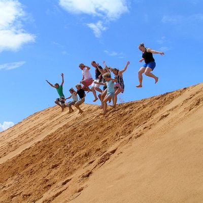 Gezin springt van een zandduin in Vietnam tijdens een familiereis, met blauwe lucht op de achtergrond.