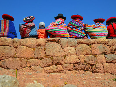 Mensen in kleurrijke poncho’s en hoeden op een stenen muur in Peru, Route Peru.