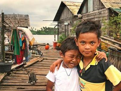 Twee kinderen op een houten pier bij paalwoningen aan het water in Zuid-Thailand.