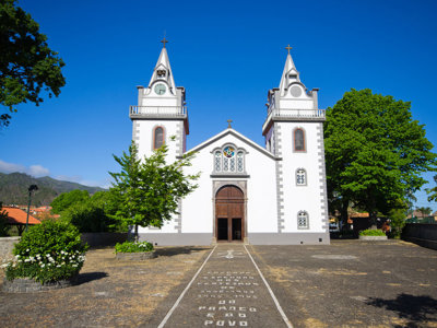 Witte kerk met twee torens op Madeira, omringd door groen onder een heldere blauwe lucht.