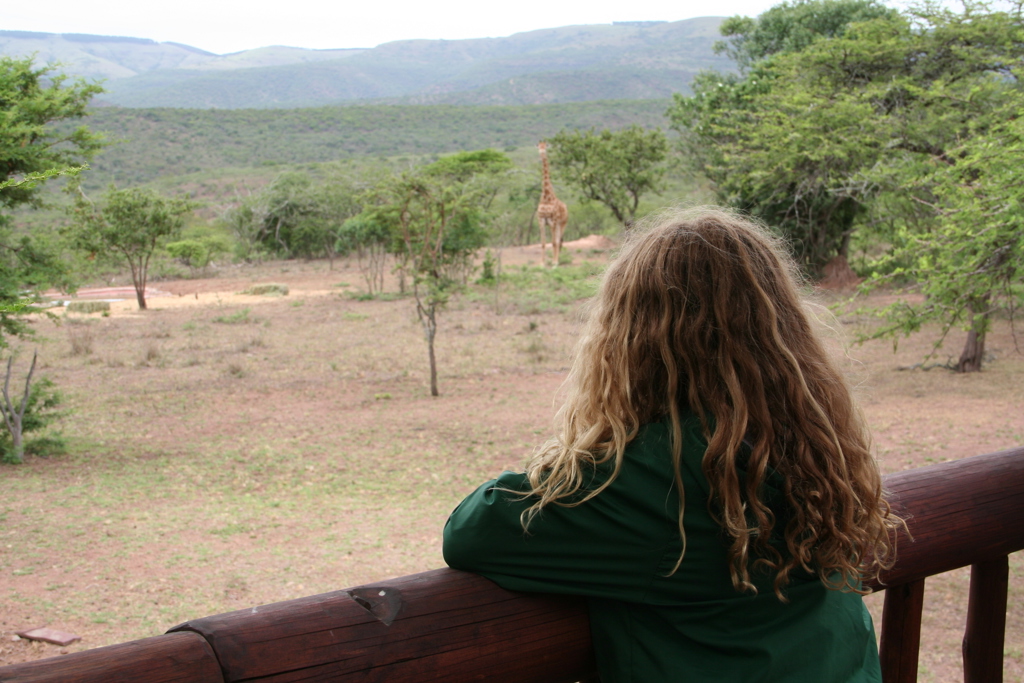 Kind kijkt vanaf een lodge-terras naar een giraffe in een wildpark tijdens familiereis Zuid-Afrika en eSwatini.
