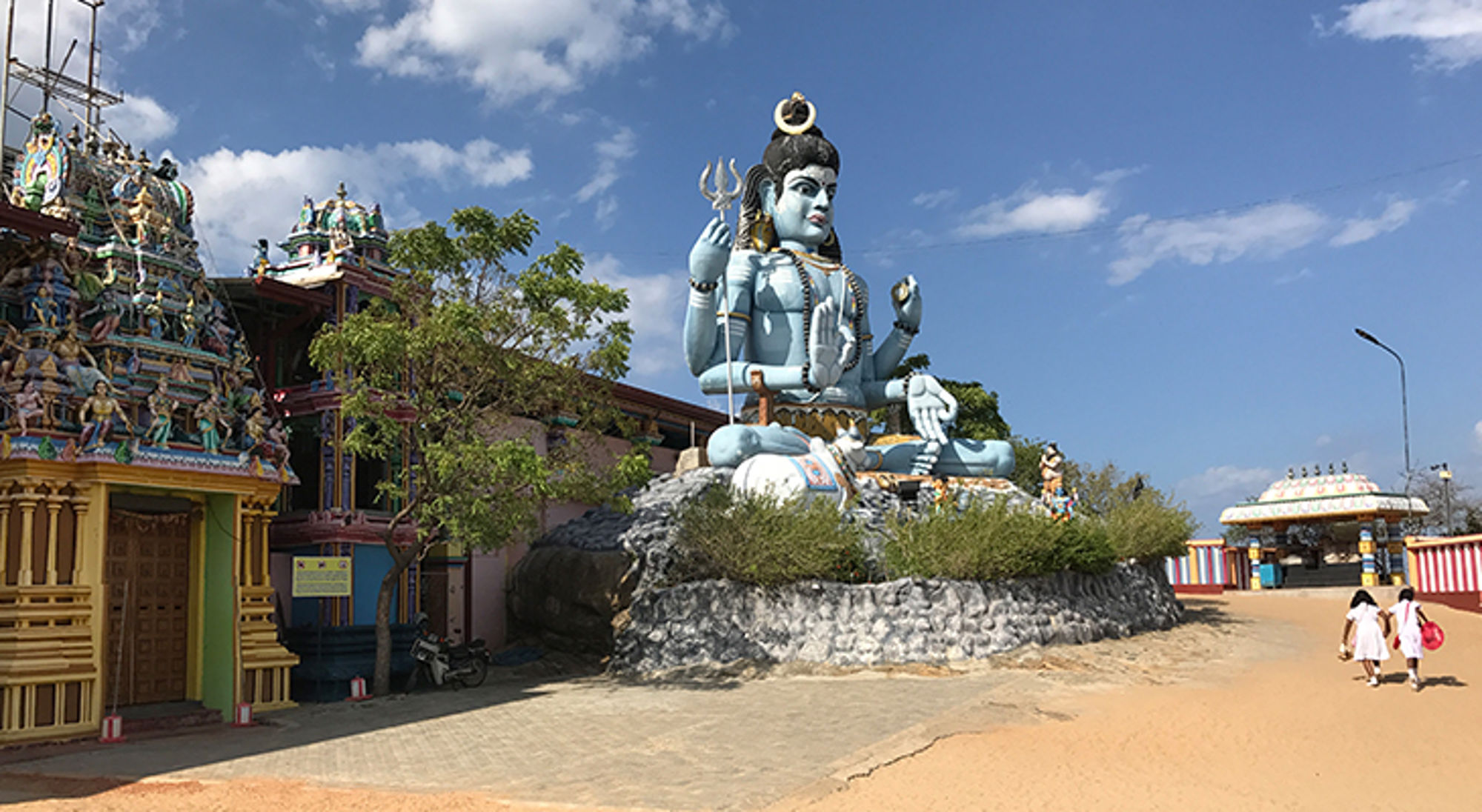 Groot Shiva-beeld bij een kleurrijke hindoeïstische tempel onder een blauwe lucht.