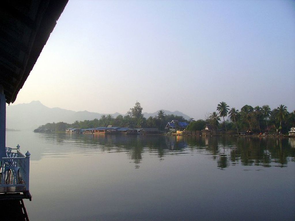 Rivierlandschap in Thailand met palmbomen en bergen in de verte, gezien vanaf een drijvend hotel.