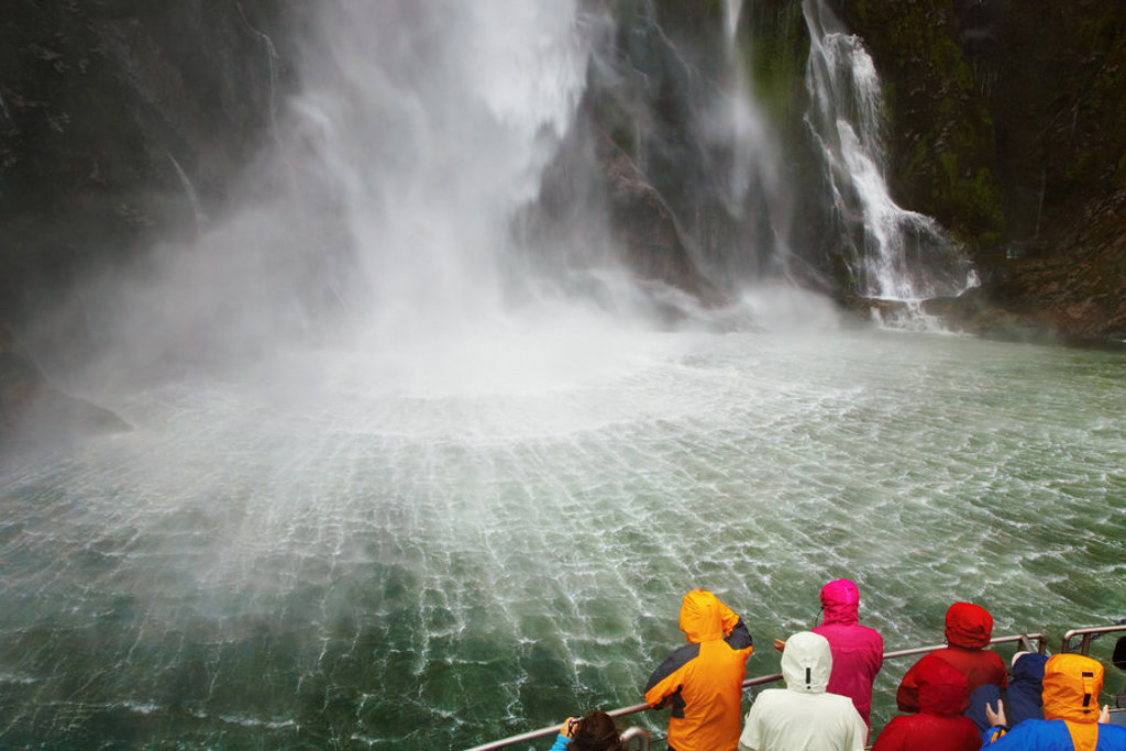 Reizigers op een boot bij een indrukwekkende waterval in Nieuw-Zeeland tijdens een groepsrondreis.