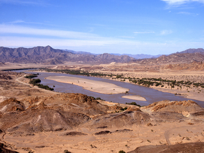 Panoramisch uitzicht op de Orange River door een droog woestijnlandschap met bergen op de route Kaapstad–Victoria Falls.