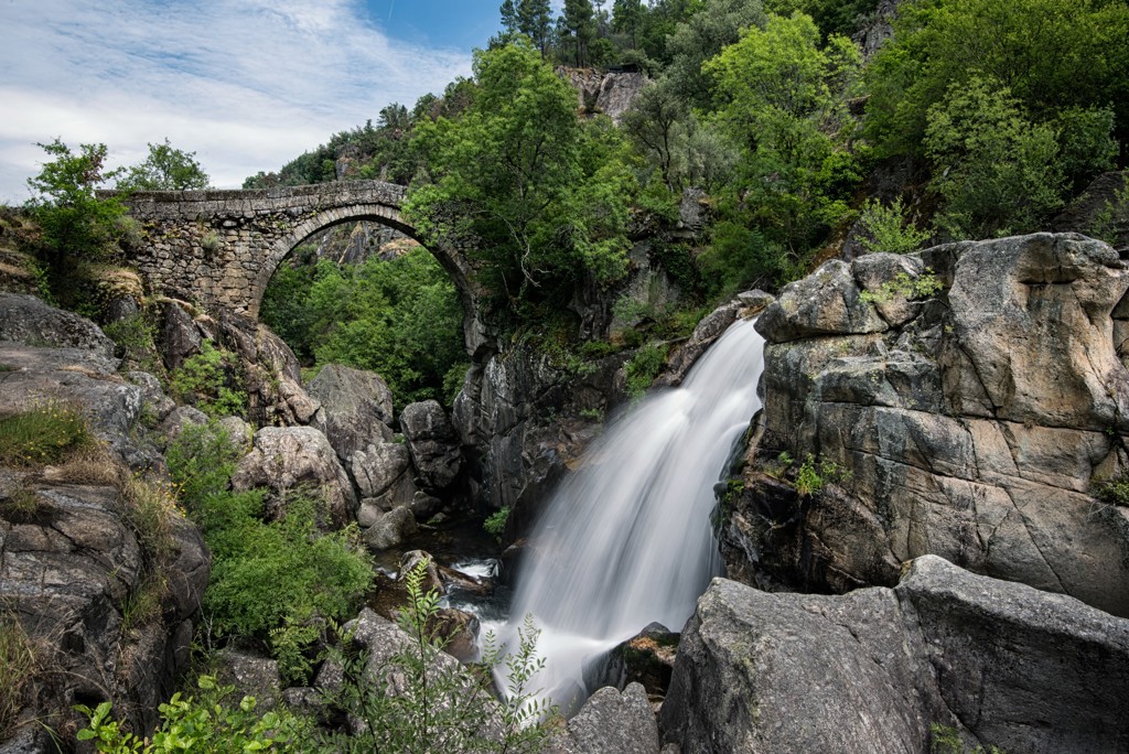 Stenen boogbrug bij waterval in een groene kloof tijdens familiereis Spanje & Portugal.
