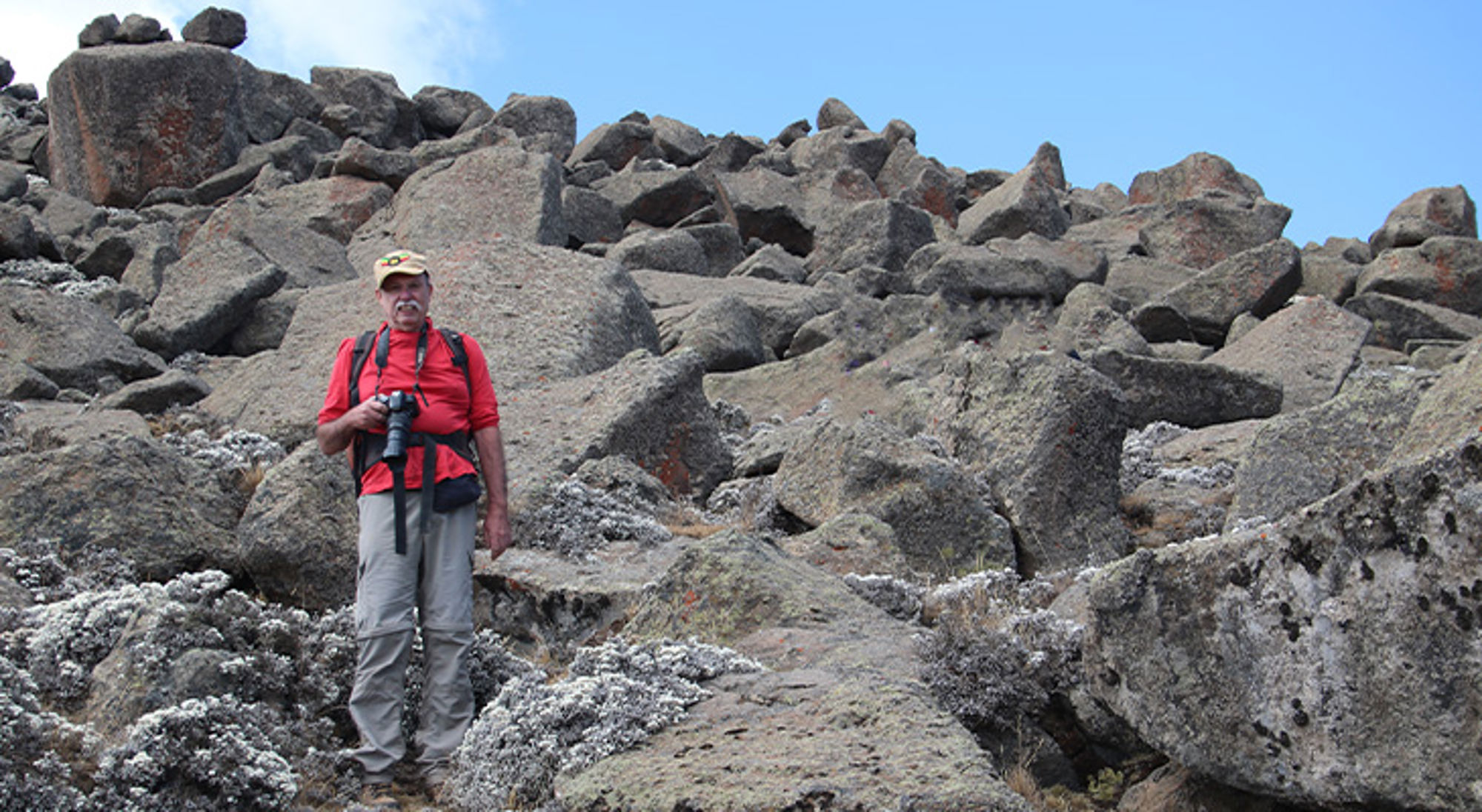 Paul in Ethiopië Wandelaar met camera tussen grote rotsblokken in berglandschap onder blauwe lucht.