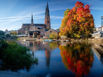 Uitzicht op de Domkerk van Uppsala aan de rivier, met herfstkleuren en spiegeling in het water tijdens Route Scandinavië.