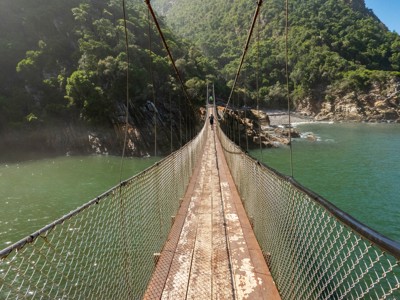 Hangbrug over een riviermonding aan de Tuinroute tussen Kaapstad en Johannesburg, met groen begroeide heuvels.
