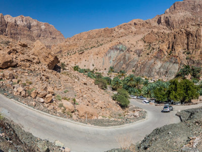 Bochtige bergweg door rotsachtig landschap in Oman, met palmoase in de vallei.