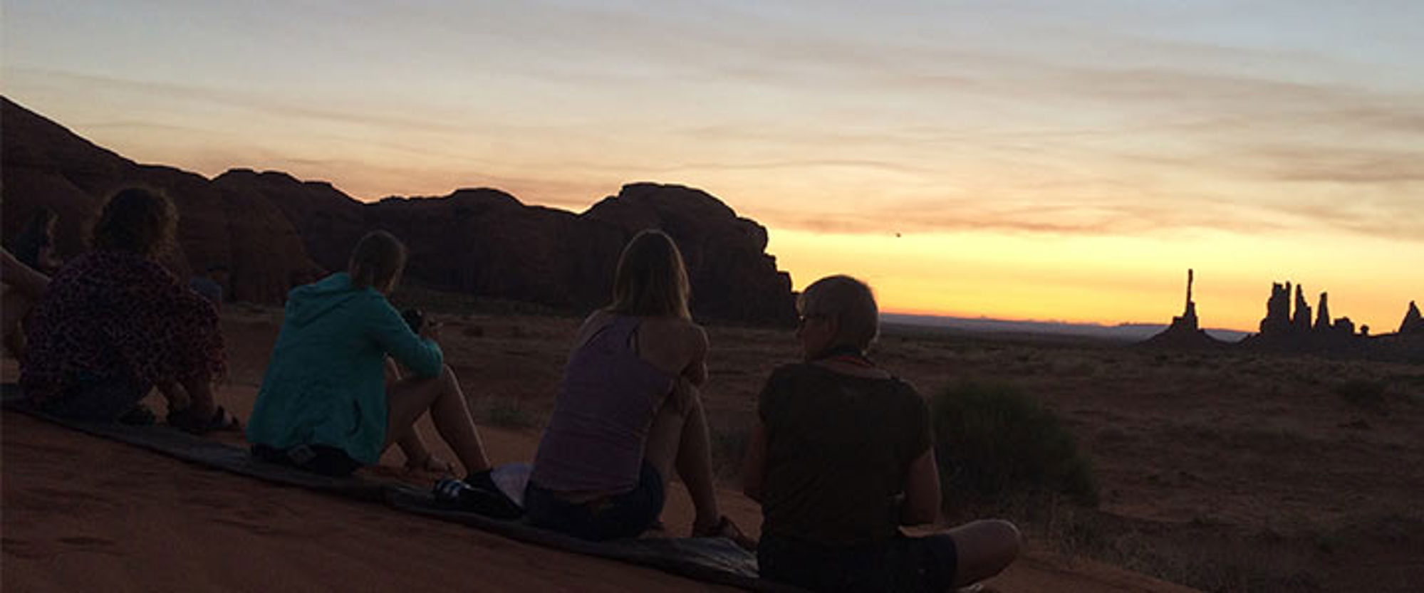 Reizigers kijken naar de zonsondergang boven Monument Valley met rotsformaties op de horizon.