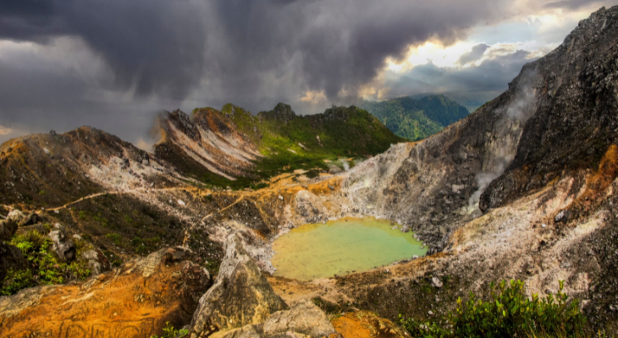 Mount Sibayak op Sumatra Kratermeer met groen water en rokende vulkanische rotsen onder dreigende wolken.