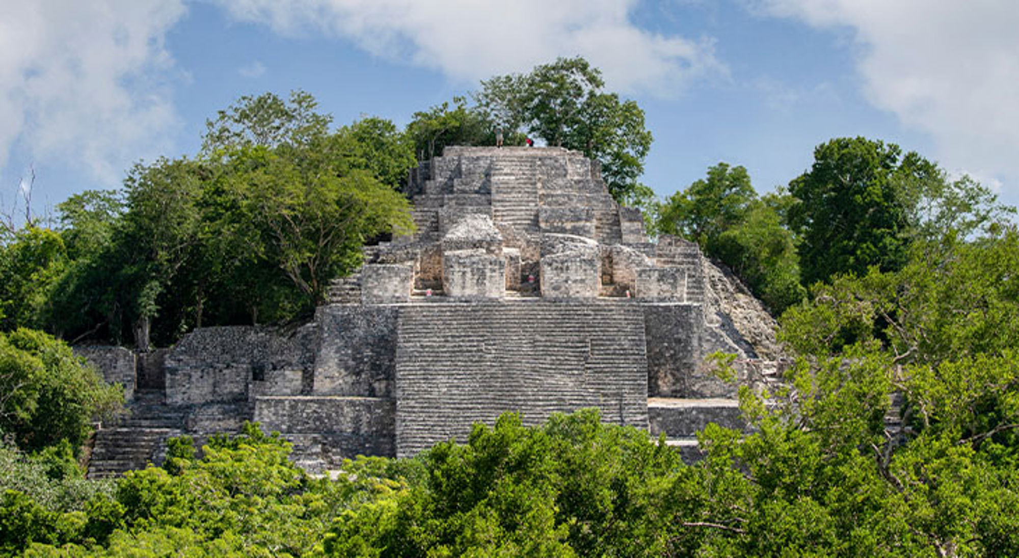 Calakmul Maya-tempelruïne in de jungle, gezien vanaf de voet van de piramide onder een blauwe lucht.