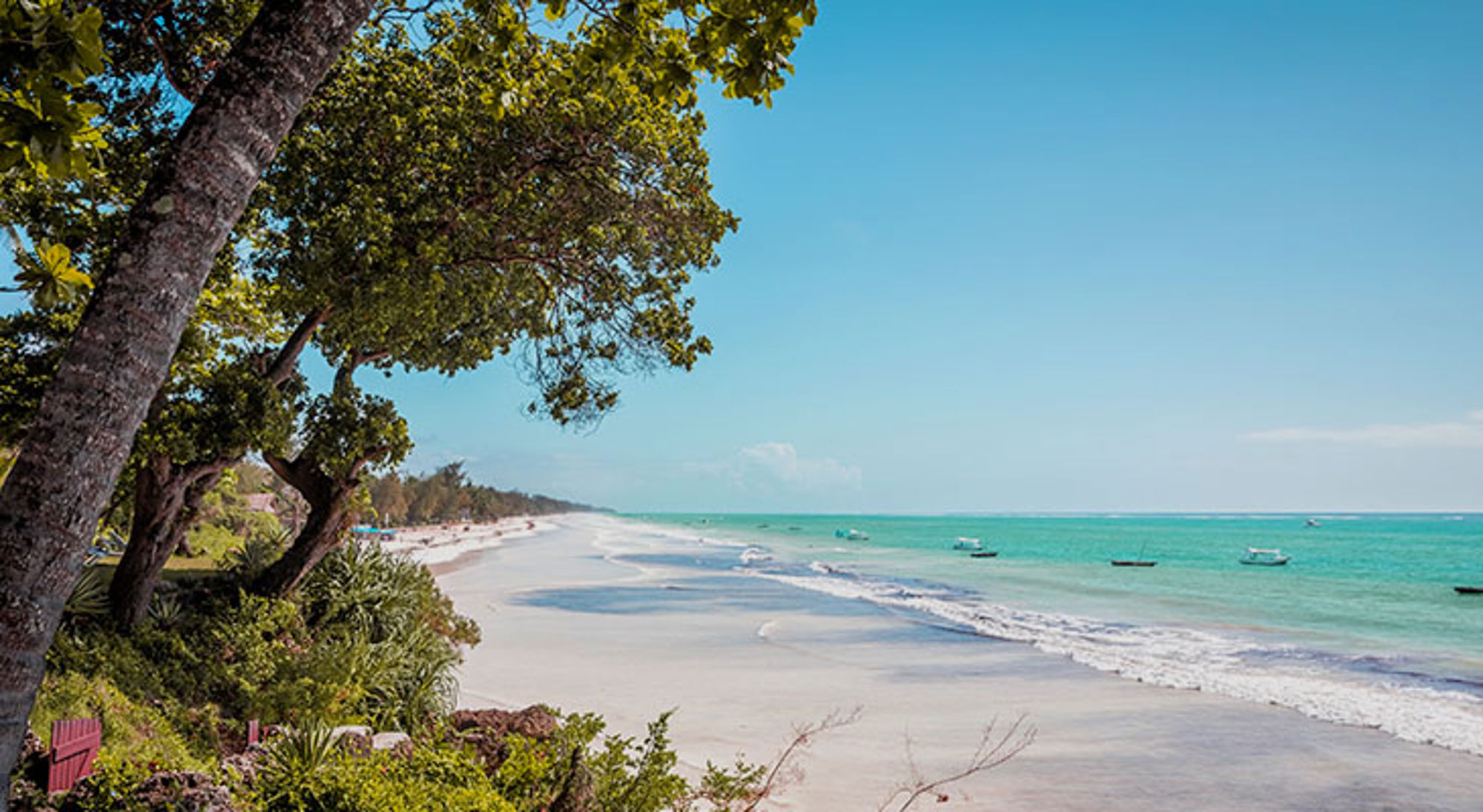 Diani Beach Wit zandstrand aan de Keniaanse kust met turquoise zee, palmbomen en bootjes voor de kust.