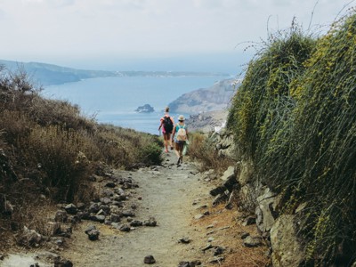 Wandelaars op een rotsachtig pad met uitzicht op de caldera en zee bij Santorini tijdens de wandelvakantie.