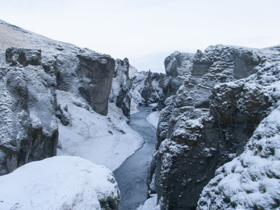 Besneeuwde kloof met rivier tussen steile rotswanden in IJsland tijdens de winterroute.