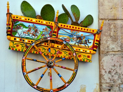 Gekleurde Siciliaanse kar en wiel als wanddecoratie met cactus, Route West Sicilië.