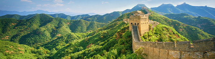 De Chinese Muur slingert door groene bergen onder een blauwe lucht, symbool van reizen in China.