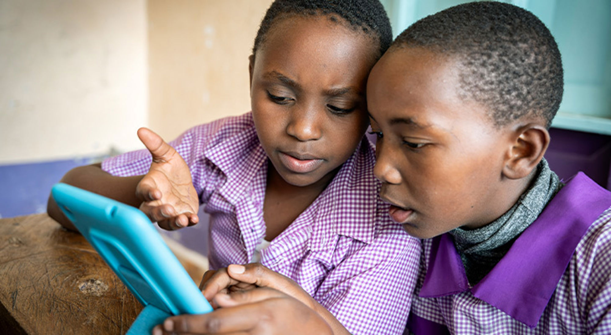 Donatie DEAN Twee scholieren in paars geruite uniformen bekijken samen een tablet in de klas.