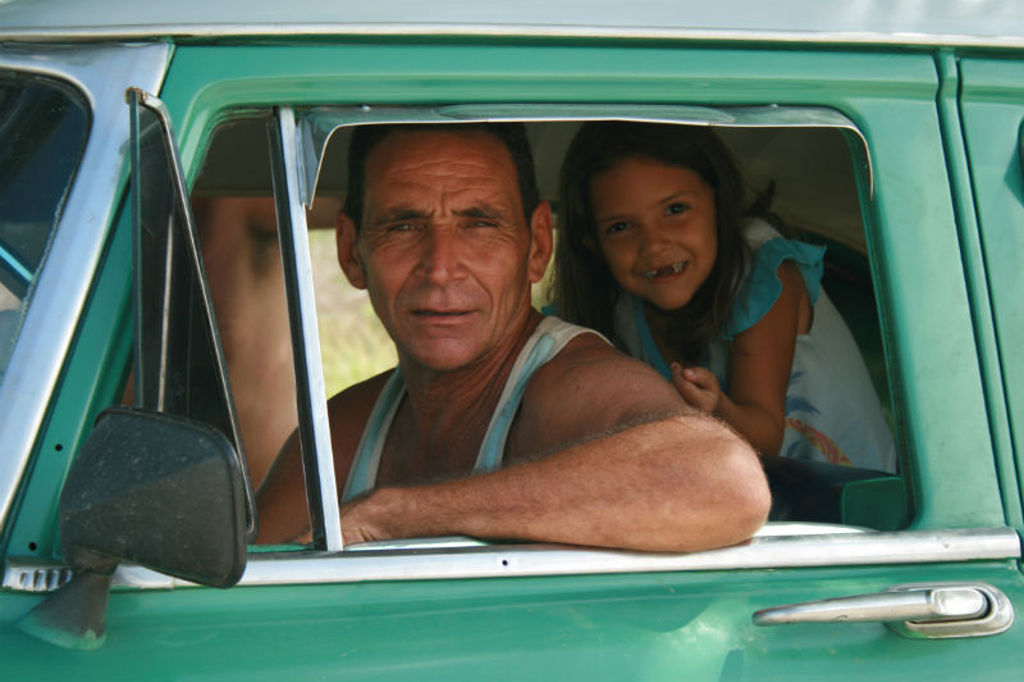 Man en meisje kijken uit het raam van een groene oldtimer in Cuba tijdens familiereis Cuba Hoogtepunten.