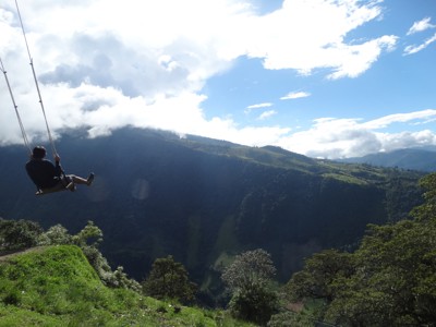 Schommel met uitzicht over de groene Andesvallei in Ecuador, onder een blauwe lucht met wolken.