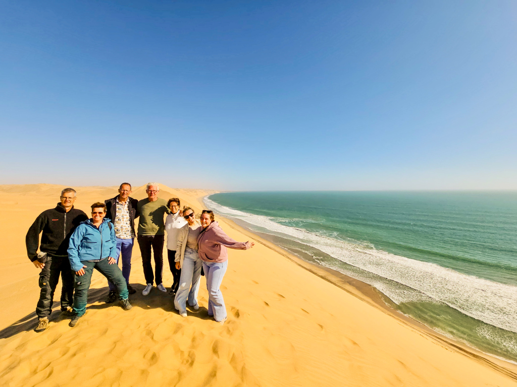Groepsrondreis Zuidelijk Afrika: reizigers op zandduin met uitzicht op de Atlantische Oceaan in Namibië.