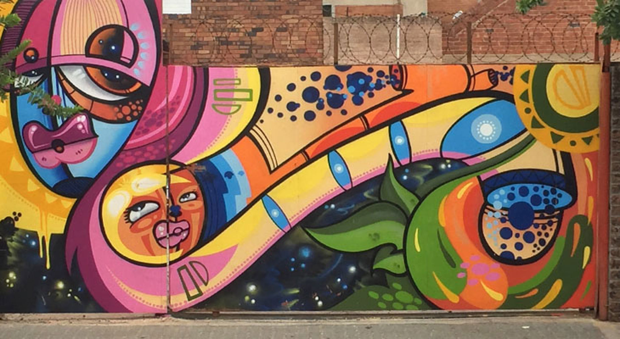 Street art Johannesburg Kleurrijke street art muurschildering met abstracte gezichten en fruit op een bakstenen muur.