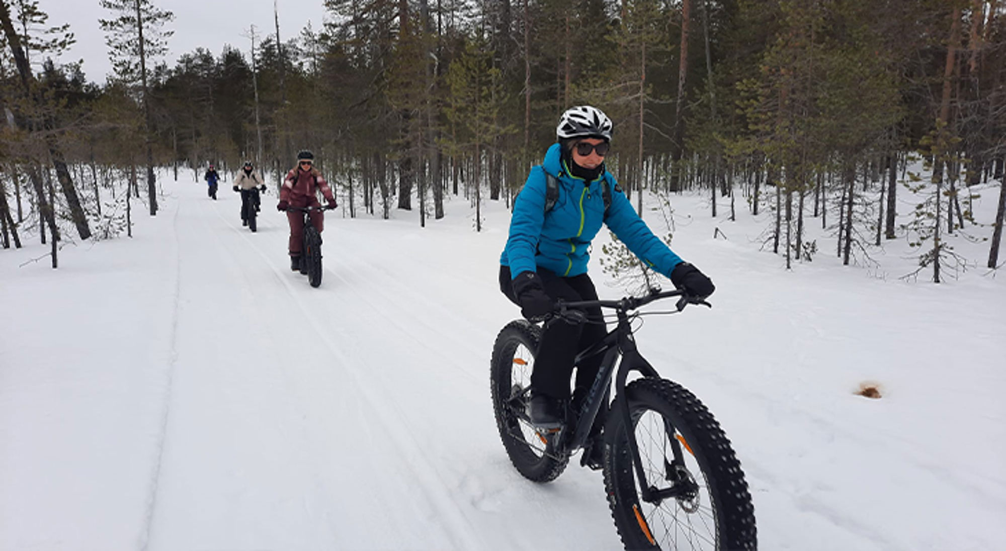 Fatbiken Finland Fatbike-tocht door een besneeuwd bos, met fietsers op een winterpad.