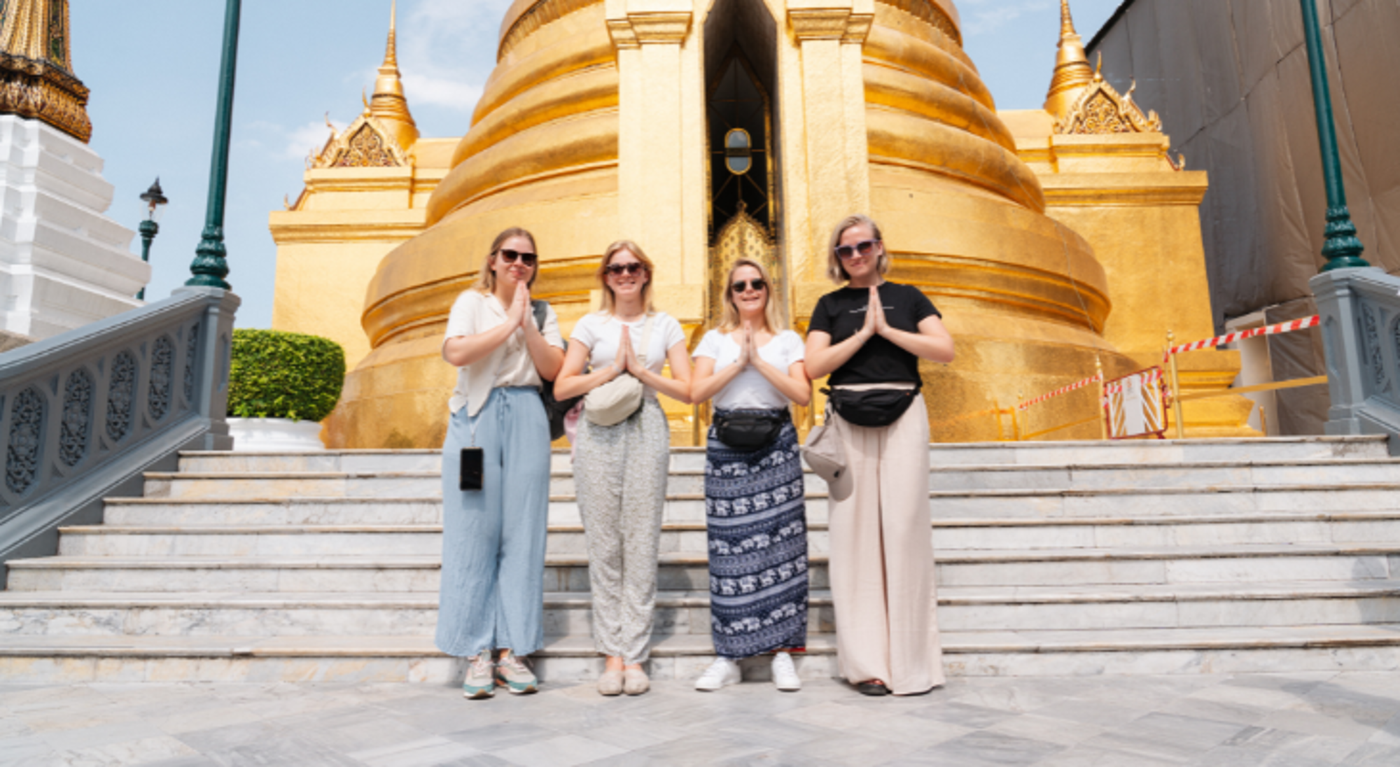 Poseren voor tempel Vier reizigers poseren met wai-groet voor een gouden tempel in Bangkok.
