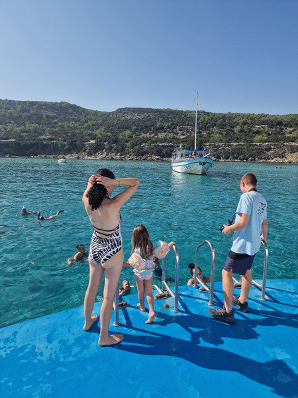 Gezin springt vanaf een boot het heldere zeewater in tijdens een familiereis op Cyprus.