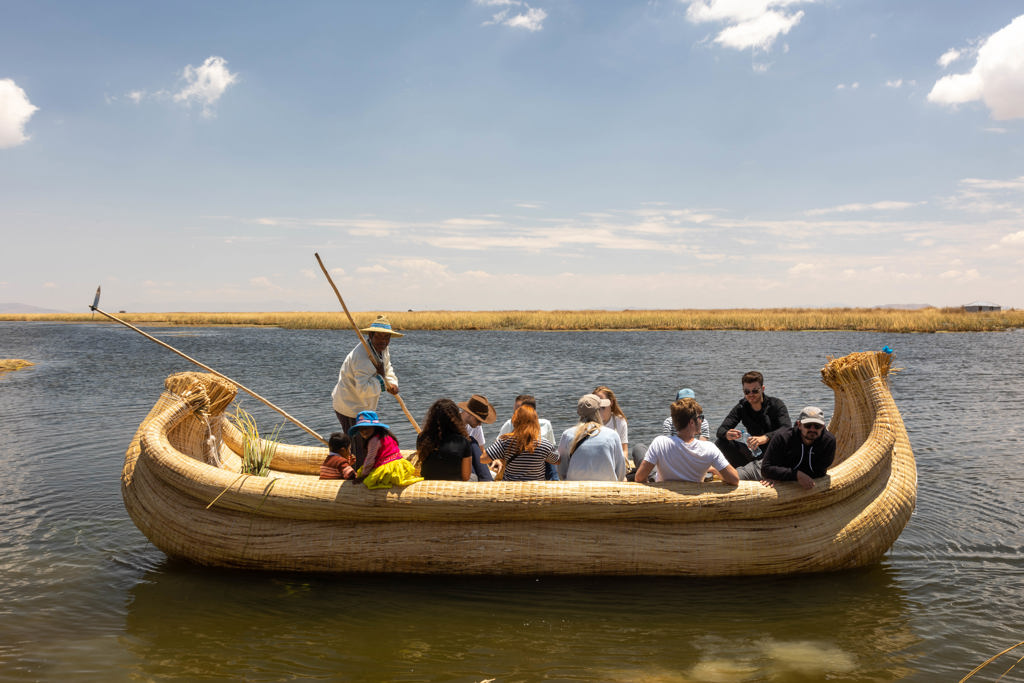 Groep reizigers vaart op een rieten boot over het Titicacameer tijdens een 22-35ers rondreis Peru.