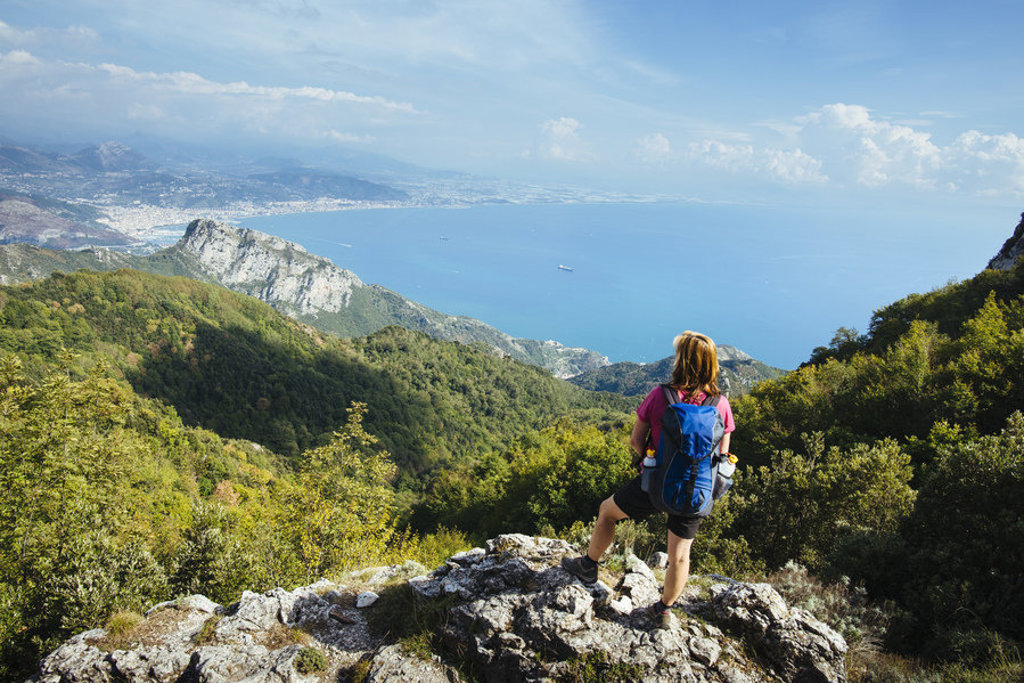 Wandelaar met rugzak kijkt uit over de Amalfikust en de Tyrreense Zee tijdens een wandelvakantie in Italië.