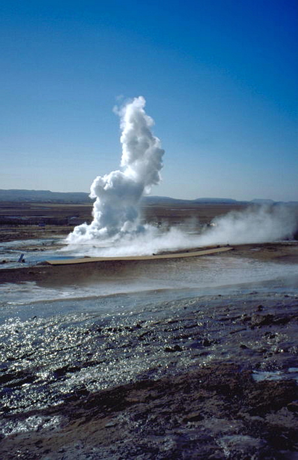 Geysir die een hoge stoompluim uitblaast in het geothermische landschap van IJsland.