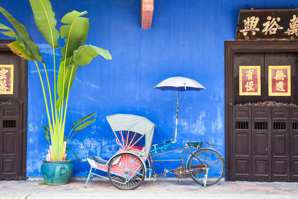 Riksja voor een blauw geschilderde gevel met Chinese decoraties in George Town, Penang, Maleisië.