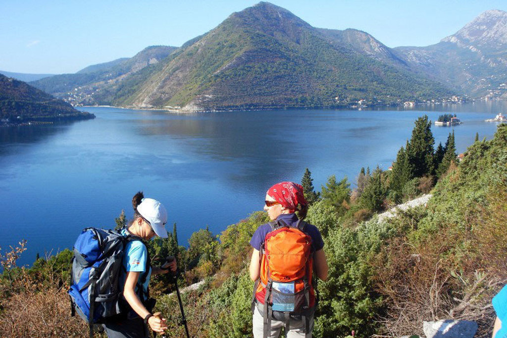 Wandelaars met rugzakken langs de Baai van Kotor met uitzicht op bergen en blauw water tijdens groepsrondreis Balkan.