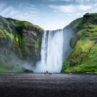 Waterval Skógafoss in IJsland, omringd door groene kliffen en zwart lavazand.