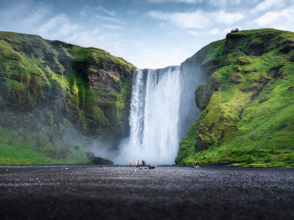 Waterval Skógafoss in IJsland, omringd door groene kliffen en zwart lavazand.