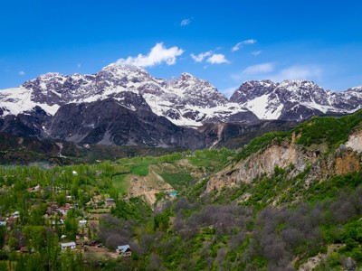 Besneeuwde bergtoppen boven een groene vallei met dorpjes in Kirgistan.