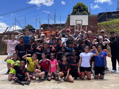 Groepsfoto met lokale jeugd en reizigers op een basketbalveld tijdens de route door Colombia.