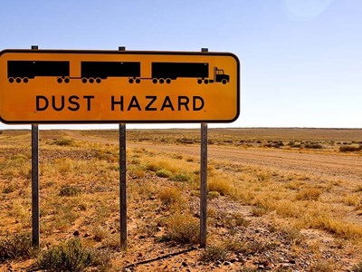 Verkeersbord met waarschuwing ‘Dust hazard’ langs een onverharde weg in de Australische outback.