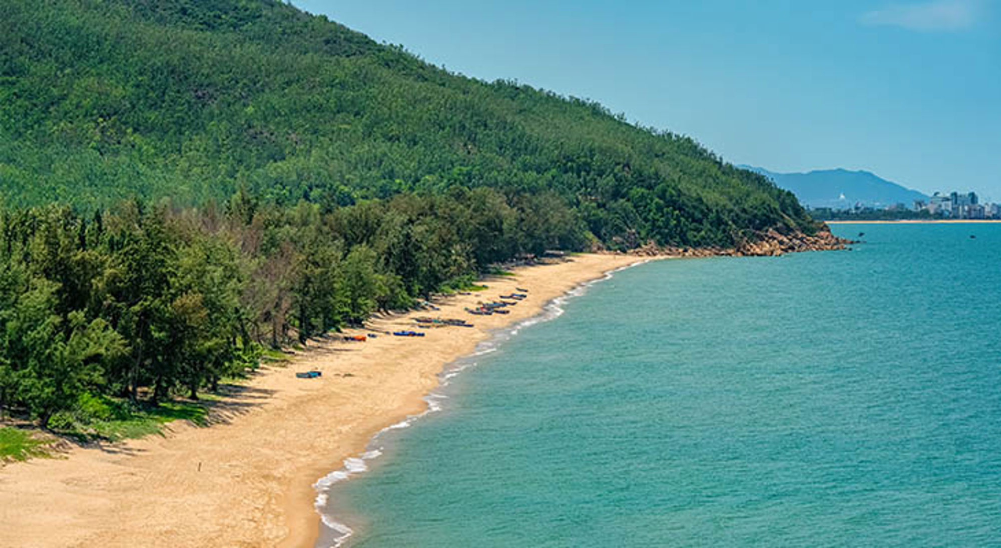 Lang zandstrand met turquoise zee en groene heuvels langs de kust in Vietnam.