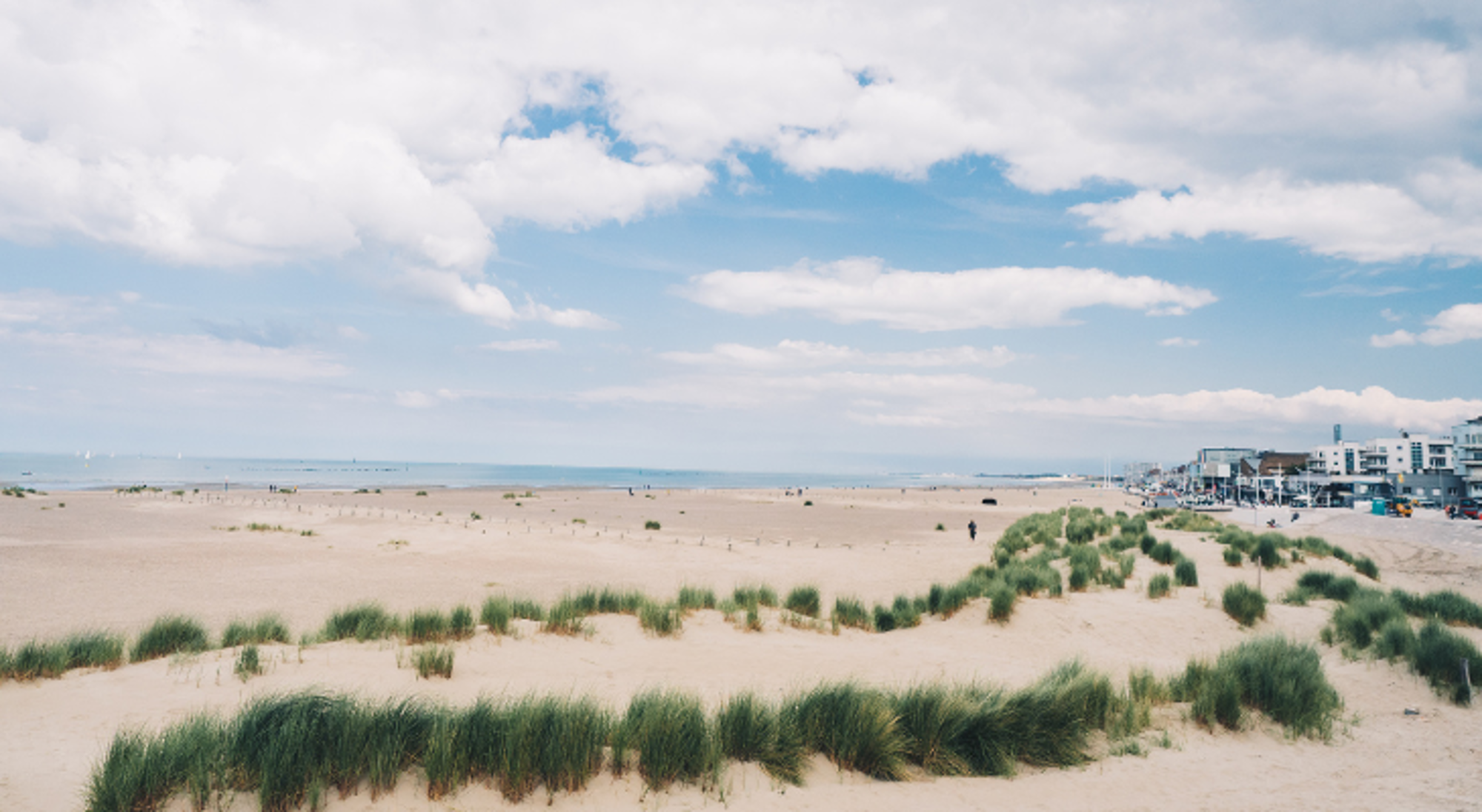 Nederland Urk Duinen met helmgras en breed zandstrand aan zee bij een kustplaats, onder een blauwe lucht met wolken.