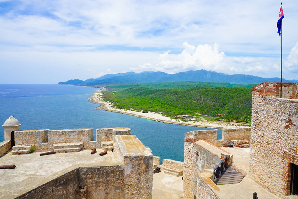 Uitzicht vanaf een fort op de Caribische kustlijn van Cuba met zee, strand en groene heuvels.