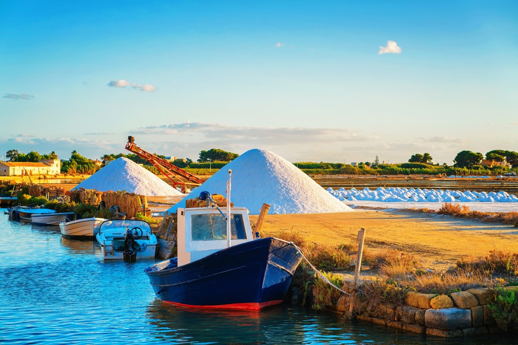 Vissersboot bij de zoutpannen van Marsala in West-Sicilië, met witte zoutbergen op de achtergrond.